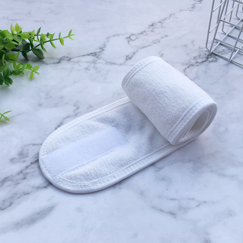 White soft terry cloth beauty headbands for women rolled on marble surface with plant decoration