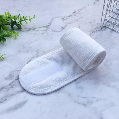 White soft terry cloth beauty headbands for women rolled on marble surface with plant decoration