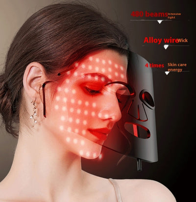 Woman wearing a black LED light therapy mask emitting red light beams for skin care