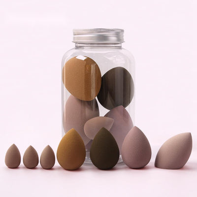 Set of various sized spherical makeup sponge in neutral colors displayed in front of a clear jar with a silver lid