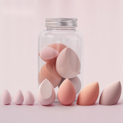 Assorted sizes and colors of spherical makeup sponge displayed in front of a clear jar with a silver lid