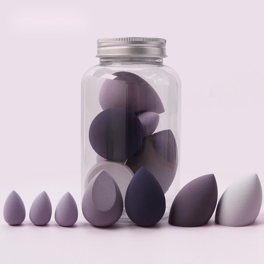 Set of purple and gray spherical makeup sponge applicators in various sizes with some inside a clear jar