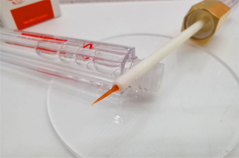 Close-up of colored mascara for eyelashes with orange applicator brush and clear tube