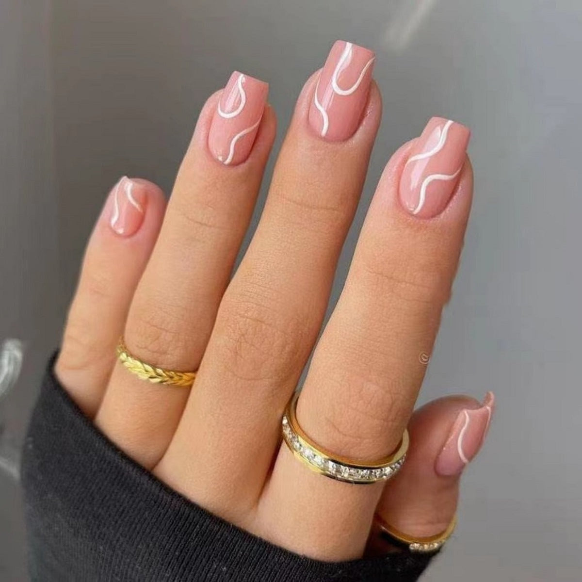 Pink press on nails for women with white abstract line design on hand wearing gold rings